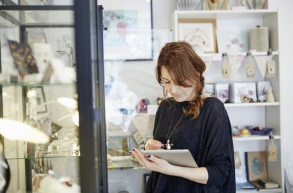 A mature woman using a digital tablet, using the touch screen, stock-taking in a small gift shop.