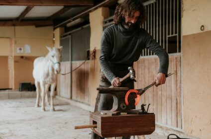 Blacksmith forging horseshoe near stable