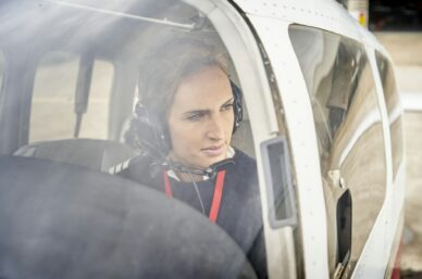 Front view from outside of a female pilot in the cockpit of an airplane.