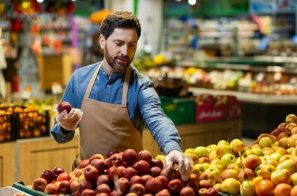 Male grocer arranging apples in produce section of grocery store