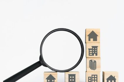 Property icons on wooden cubes with magnifying glass. Concept of property investment analysis.