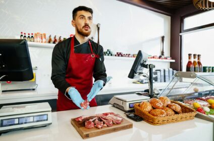 Young butcher holding raw lamb ribs in a butcher shop